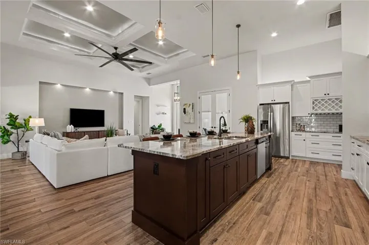 Two tone kitchen with pendant lighting, two tone cabinetry, open floor plan, a ceiling fan, and light stone counters