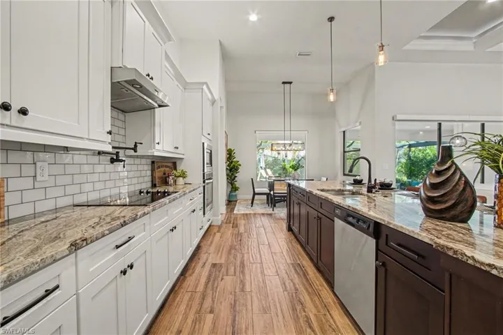 Kitchen featuring two tone cabinets, hanging light fixtures, light stone counters, stainless steel dishwasher, and light wood-type flooring