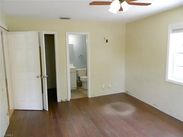 Unfurnished bedroom featuring hardwood / wood-style floors, connected bathroom, baseboards, and a ceiling fan