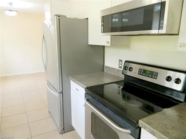 Kitchen featuring appliances with stainless steel finishes, white cabinetry, light tile patterned floors, dark countertops, and baseboards