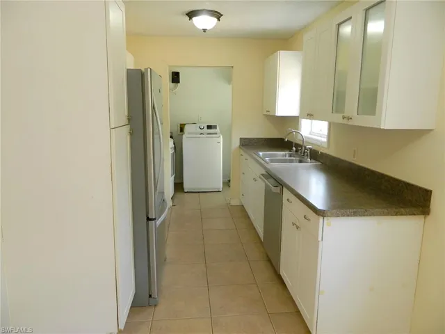 Kitchen with washer / clothes dryer, a sink, stainless steel appliances, dark countertops, and white cabinets