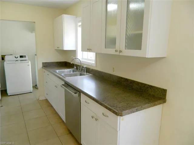 Kitchen with washer / dryer, a sink, dishwasher, dark countertops, and white cabinets