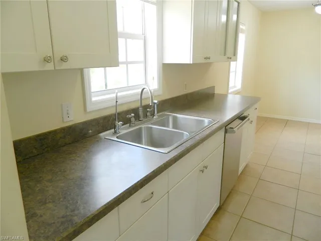 Kitchen with a sink, stainless steel dishwasher, white cabinets, light tile patterned flooring, and baseboards