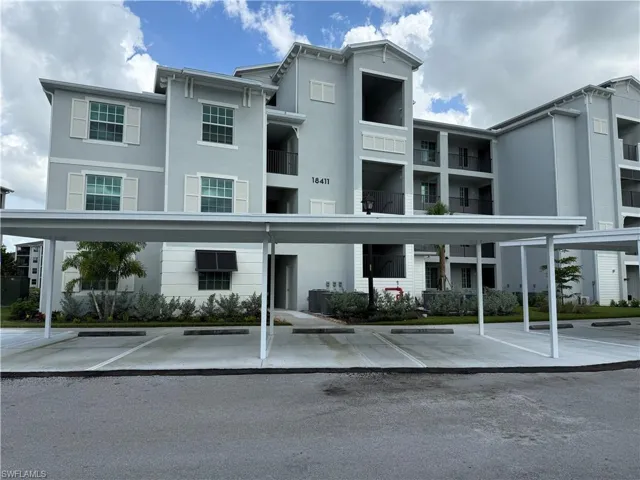 Multi-story building with multiple balconies, covered parking structures, and landscaped shrubbery