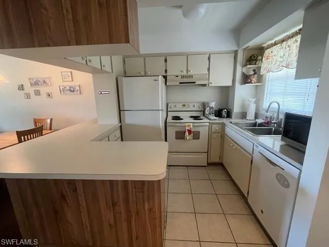 Kitchen featuring sink, white appliances, kitchen peninsula, and light tile patterned flooring