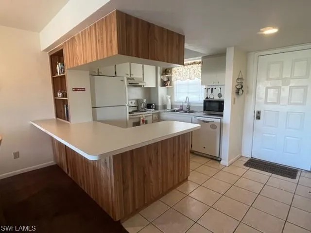 Kitchen featuring white appliances, white cabinets, sink, kitchen peninsula, and light tile patterned floors