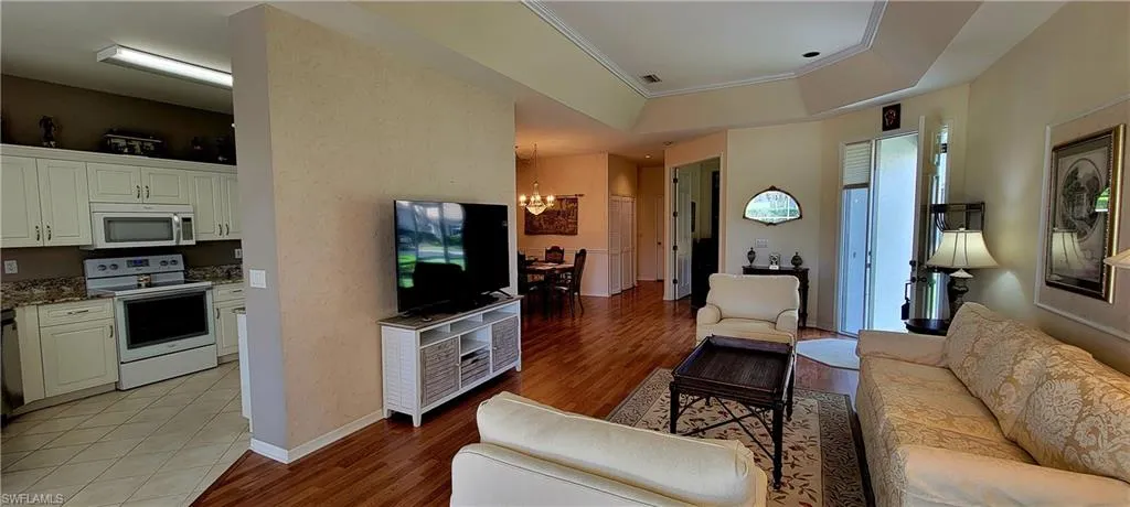 Living area featuring a chandelier, light wood-type flooring, a raised ceiling, and ornamental molding