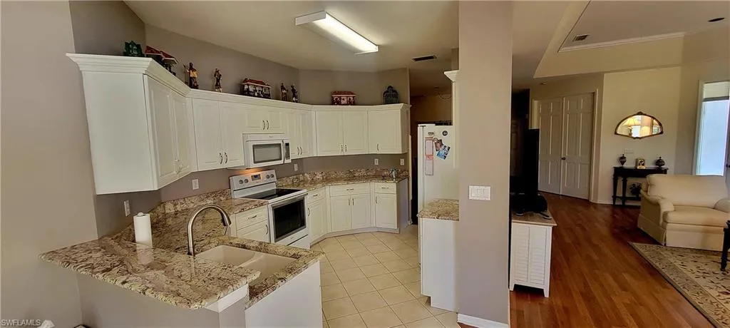Kitchen with white appliances, open floor plan, white cabinetry, light stone counters, and a peninsula