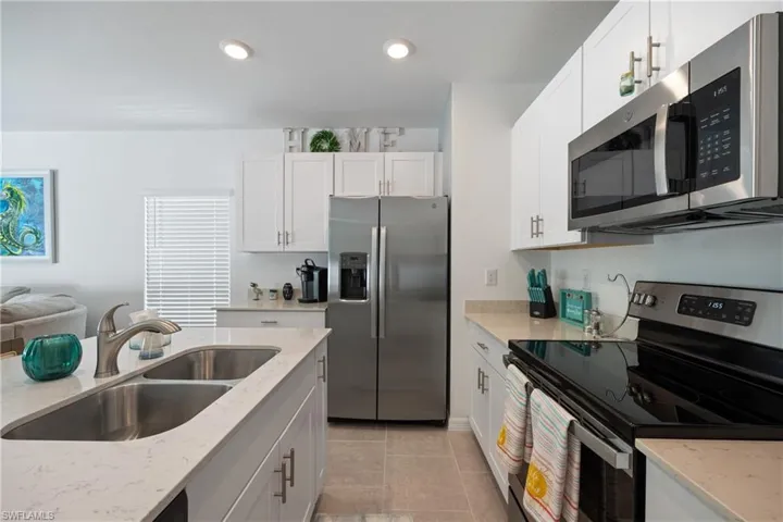 Kitchen featuring light tile flooring, white cabinetry, light stone countertops, appliances with stainless steel finishes, and sink
