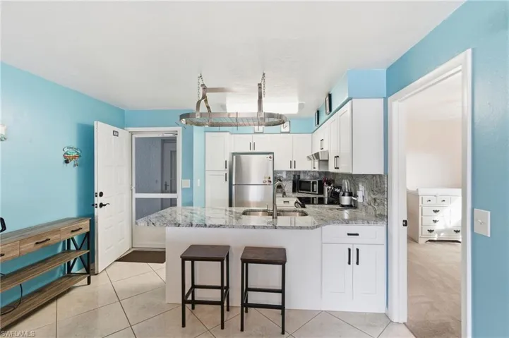 Kitchen featuring a peninsula, white cabinetry, light stone countertops, stainless steel appliances, and a kitchen bar