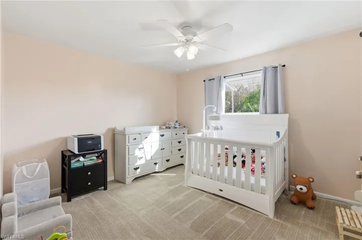 Bedroom featuring light colored carpet, a ceiling fan, and a nursery area