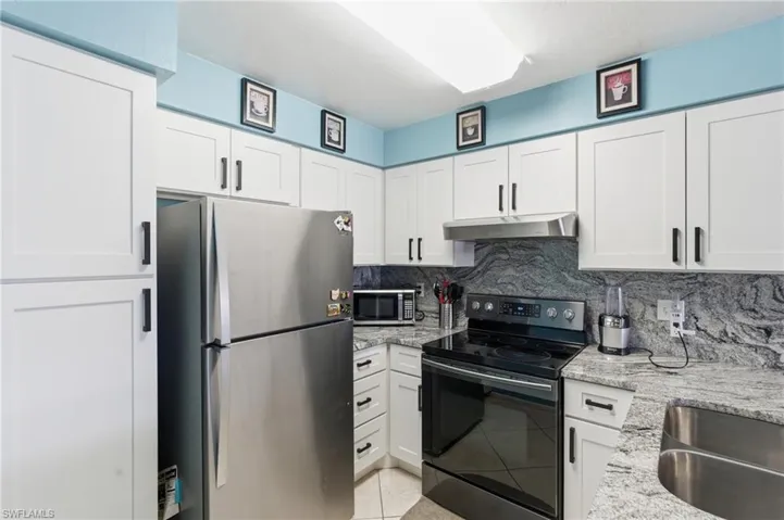 Kitchen with stainless steel appliances, white cabinets, light stone countertops, and backsplash