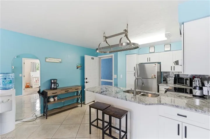 Kitchen featuring a peninsula, white cabinetry, light stone counters, stainless steel appliances, and arched walkways