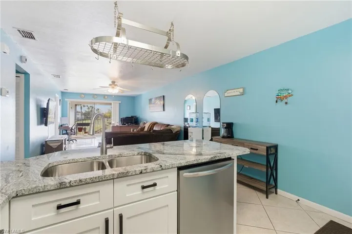 Kitchen with light stone counters, dishwasher, white cabinets, and light tile patterned flooring