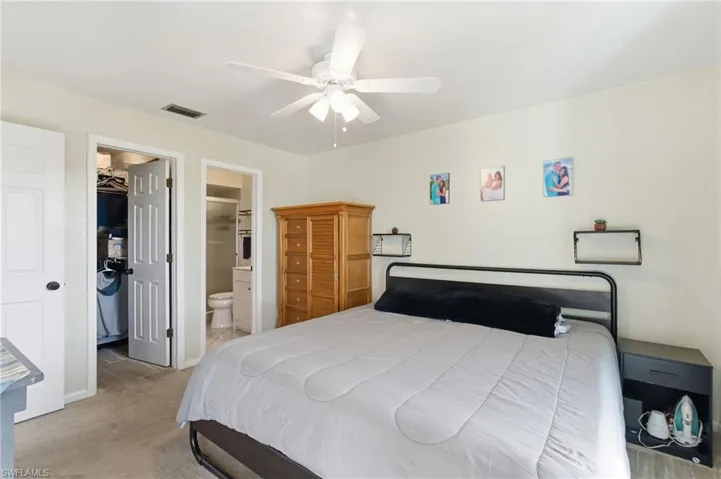 Bedroom featuring light colored carpet, a walk in closet, a ceiling fan, and ensuite bathroom