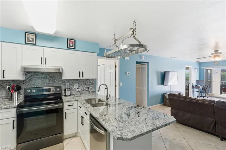 Kitchen featuring stainless steel appliances, a peninsula, light stone countertops, white cabinetry, and decorative backsplash