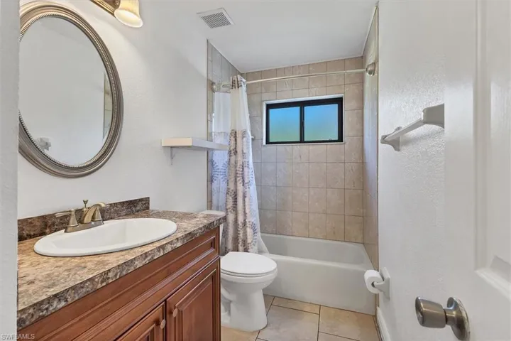 Bathroom featuring visible vents, toilet, shower / tub combo with curtain, tile patterned floors, and vanity