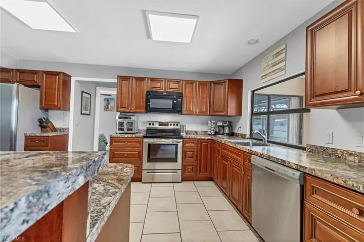 Kitchen featuring dark stone countertops, light tile patterned floors, a sink, stainless steel appliances, and brown cabinets