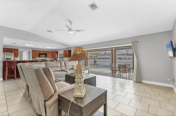 Living area with visible vents, a ceiling fan, light tile patterned flooring, baseboards, and vaulted ceiling