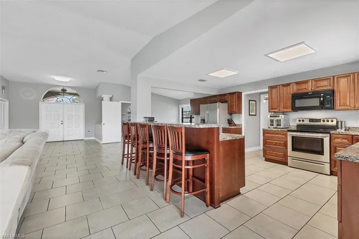 Kitchen featuring a breakfast bar, open floor plan, stainless steel appliances, light tile patterned floors, and baseboards