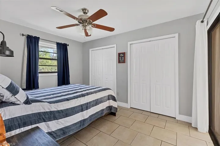 Bedroom with light tile patterned floors, baseboards, two closets, and a ceiling fan
