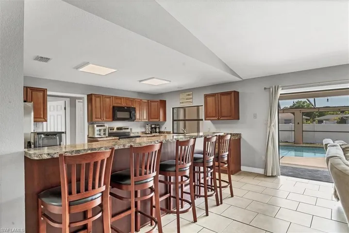Kitchen featuring visible vents, brown cabinets, appliances with stainless steel finishes, and a kitchen bar