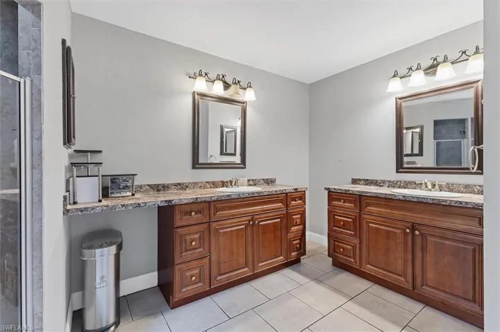 Bathroom with tile patterned floors, a stall shower, two vanities, and a sink