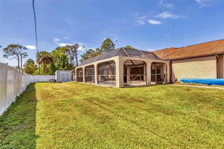 Rear view of house with glass enclosure, a lawn, a fenced backyard, an outbuilding, and a storage unit