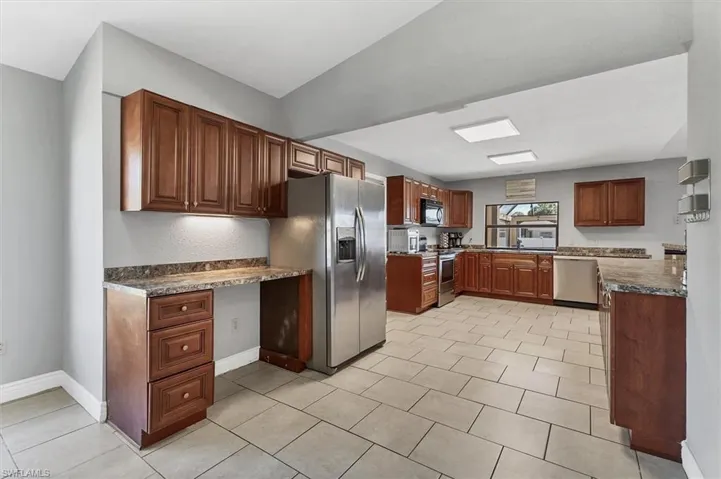 Kitchen featuring a sink, dark countertops, built in desk, stainless steel appliances, and baseboards