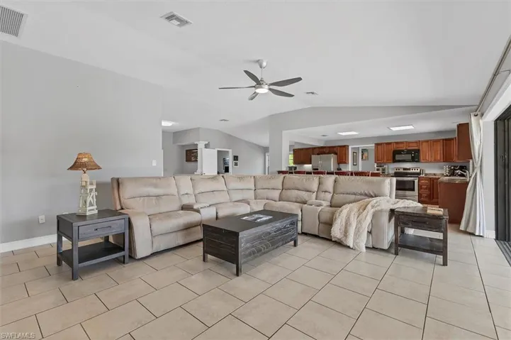 Living area with light tile patterned floors, visible vents, ceiling fan, and vaulted ceiling