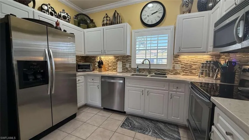 Kitchen featuring stainless steel appliances, crown molding, light tile patterned floors, tasteful backsplash, and white cabinetry