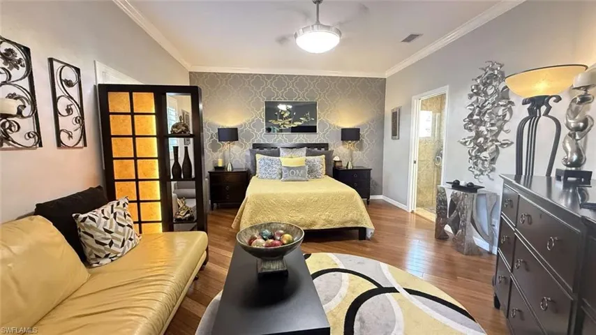 Bedroom featuring an accent wall, wallpapered walls, wood finished floors, and crown molding