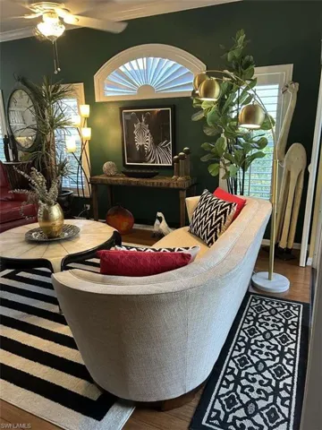 Living room with ceiling fan, wood finished floors, crown molding, and healthy amount of natural light
