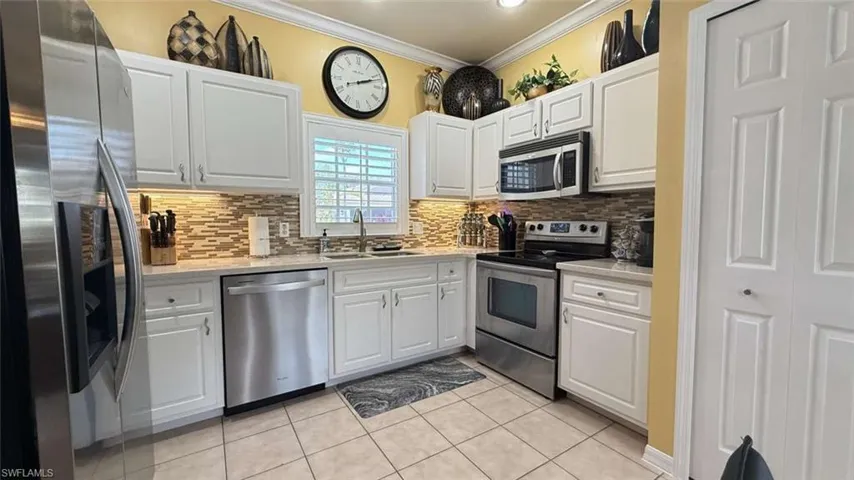 Kitchen featuring stainless steel appliances, light countertops, crown molding, backsplash, and white cabinets