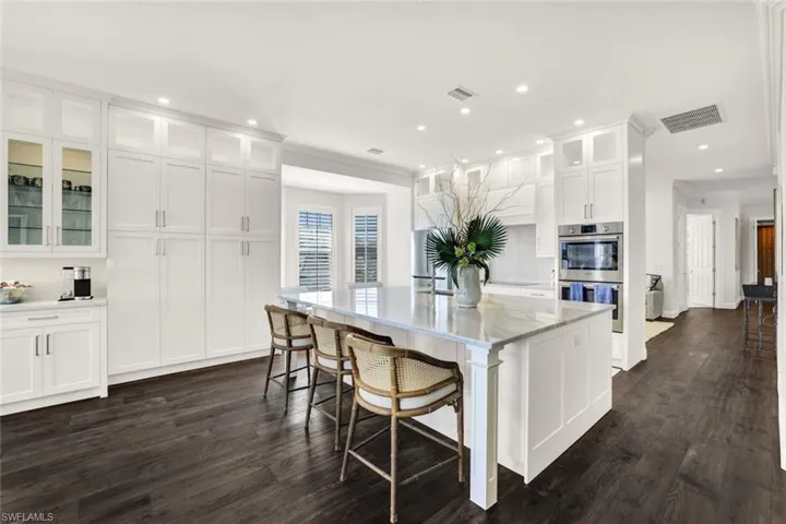 Kitchen featuring dark wood-type flooring, a breakfast bar, white cabinets, a center island with sink, and stainless steel double oven