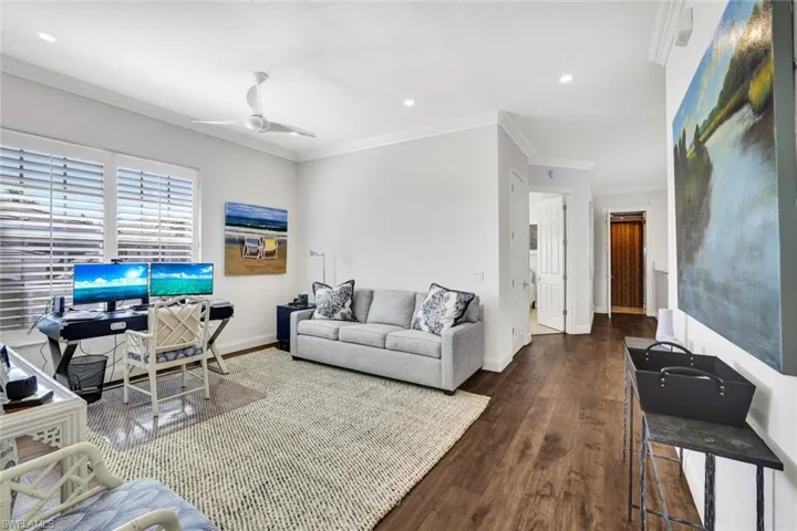 Living room featuring dark wood-type flooring, ornamental molding, and ceiling fan
