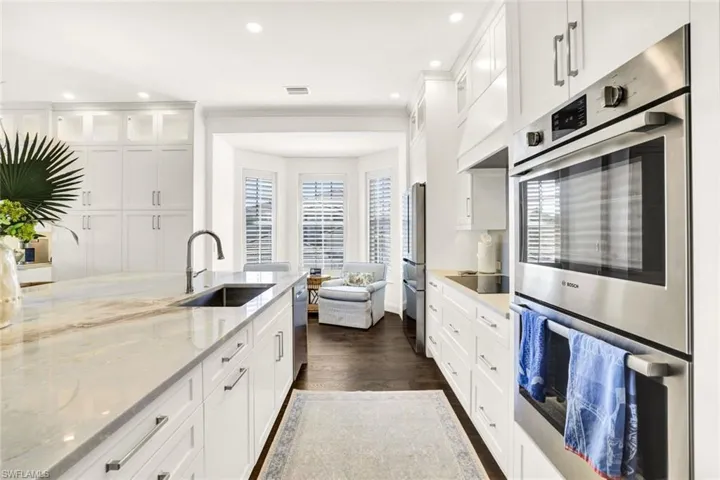 Kitchen featuring dark wood-type flooring, sink, white cabinetry, light stone counters, and appliances with stainless steel finishes
