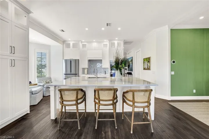 Kitchen with a spacious island, stainless steel fridge, a breakfast bar area, and white cabinets
