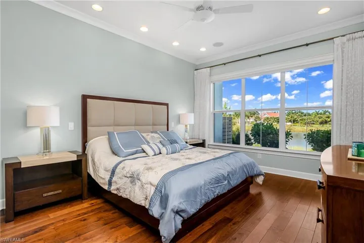 Bedroom with crown molding, a water view, hardwood / wood-style floors, and ceiling fan. Electric shades are open to show off the lovely water views.