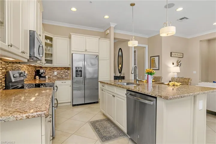 Kitchen featuring decorative light fixtures, an island with sink, stainless steel appliances, and sink.