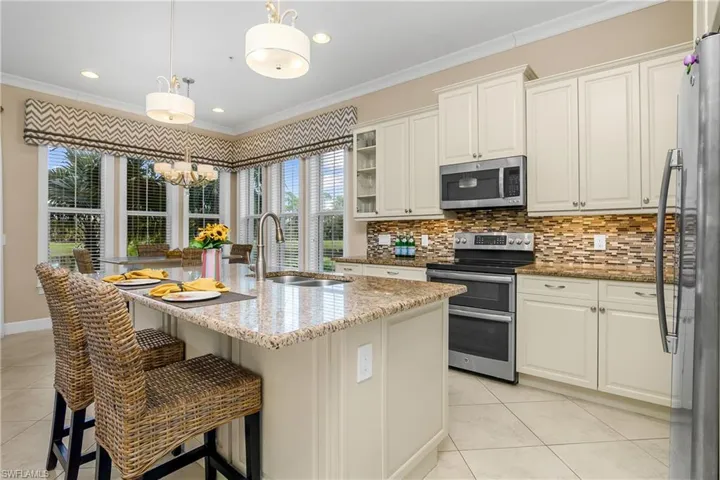 Kitchen featuring pendant lighting, sink, stainless steel appliances, a center island with sink, and light stone countertops.