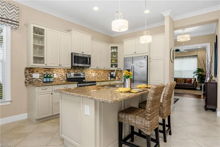 Island Kitchen with light stone counters, white cabinets, ornamental molding, stainless steel appliances, ample cabinet space. Pendant Lighting.