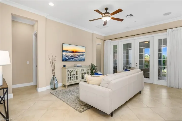 Living room with french doors that lead to the screened Lanai, light tile patterned flooring, ornamental molding, and ceiling fan. Ceiling lights and whole house speakers.