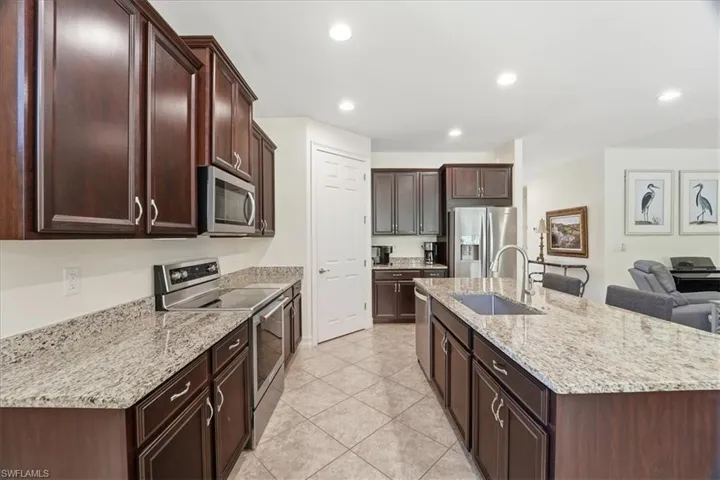 Kitchen featuring appliances with stainless steel finishes, light stone counters, dark brown cabinets, a center island with sink, and recessed lighting