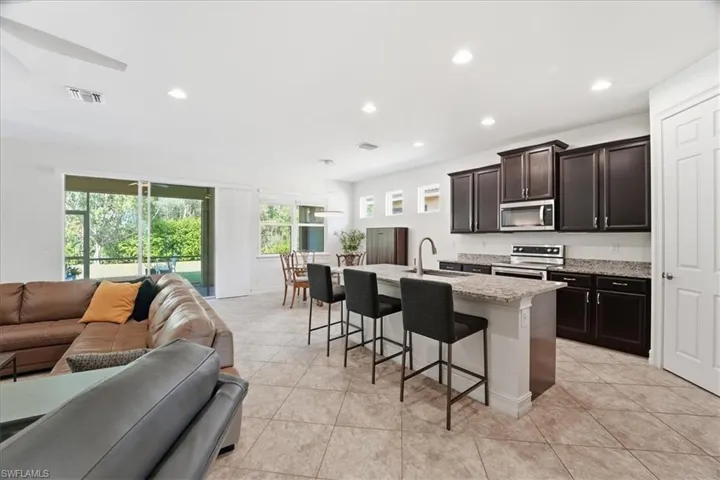Kitchen featuring open floor plan, a kitchen bar, stainless steel appliances, light stone counters, and an island with sink