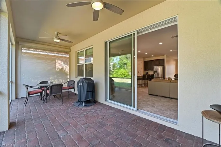 Sunroom with a textured wall, outdoor dining space, a ceiling fan, a patio, and brick flooring