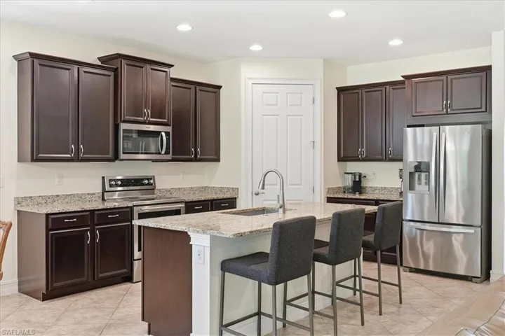 Kitchen featuring stainless steel appliances, light stone counters, dark brown cabinets, light tile patterned flooring, and recessed lighting