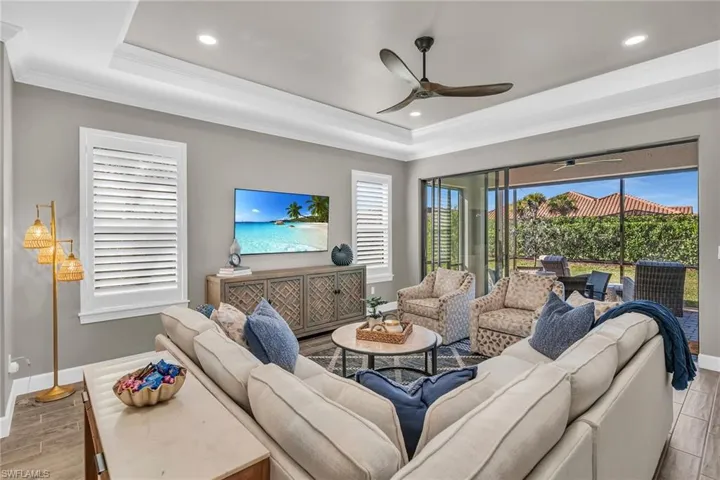 Living room featuring a tray ceiling, crown molding, a ceiling fan, wood finished floors, and baseboards