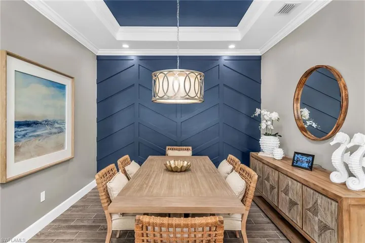 Dining room featuring wood tiled floor, visible vents, a raised ceiling, and crown molding