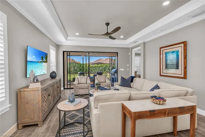 Living area with light wood-style floors, visible vents, a tray ceiling, and crown molding